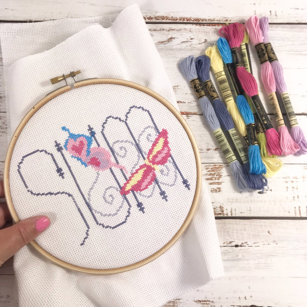 Butterfly cross stitch in progress in wooden embroidery hoop with colourful DMC embroidery threads.