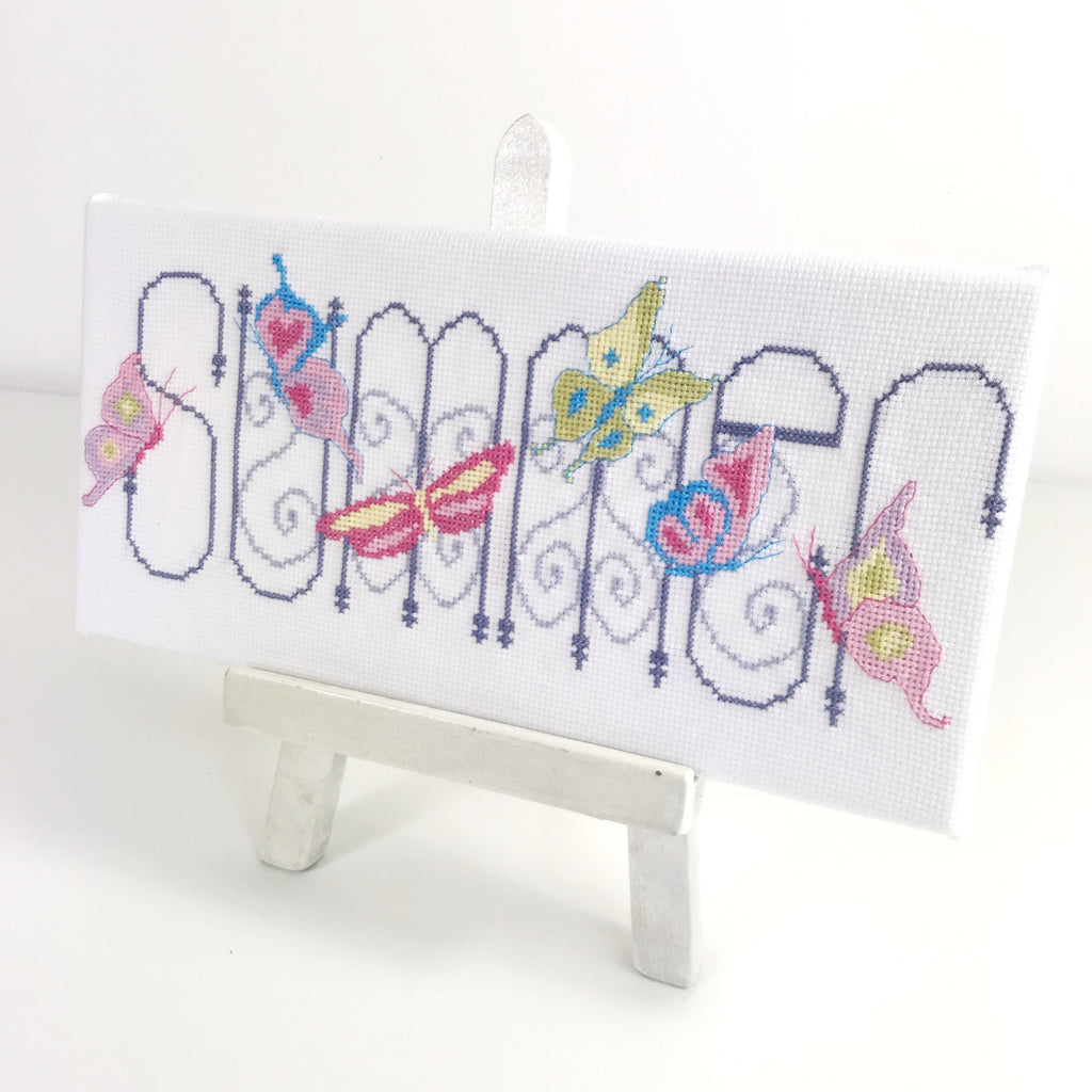 Summer cross stitch, finished on a artist canvas displayed on as artists easel.