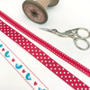 Set of three christmas themed ribbons. blue folk bird, red polka dot and a red saddle stitch with embroidery scissors and vintage reel