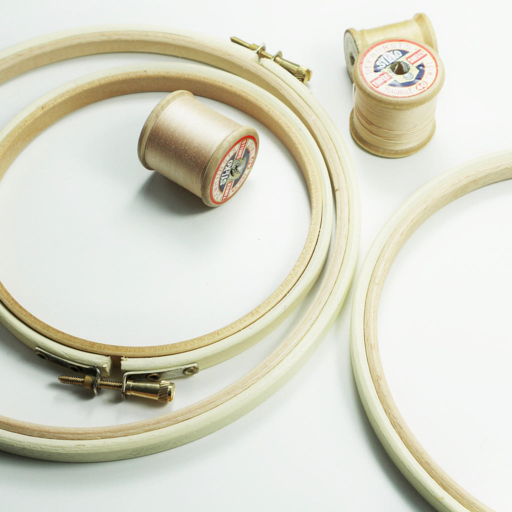Three cream coloured embroidery hoops with embroidery reels.