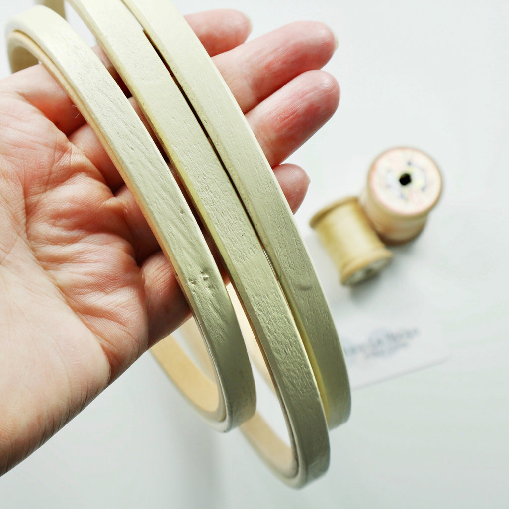 Three cream embroidery hoops being held in a hand. vintage cotton reels in the distance.