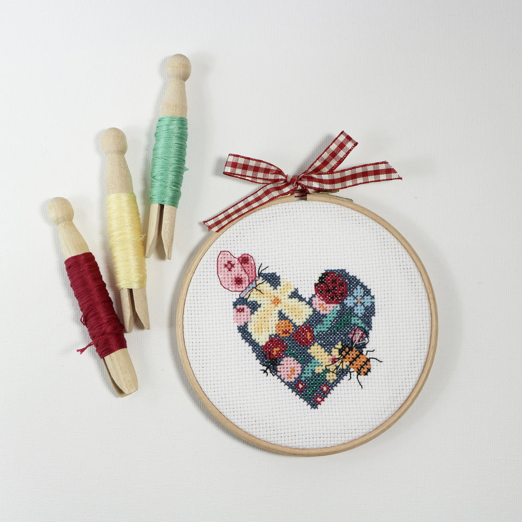 Love heart cross stitch in embroidery hoop with threads on pegs.