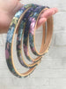 Stack of floral-patterned embroidery hoops held by a hand on a light background