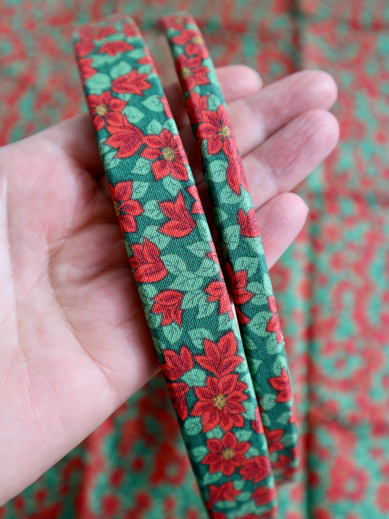 Hand holding two green embroidery hoops with red floral patterns against a patterned background
