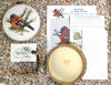 Embroidery kit with cross-stitched bird design, hoop, and pattern sheet on a floral fabric background.