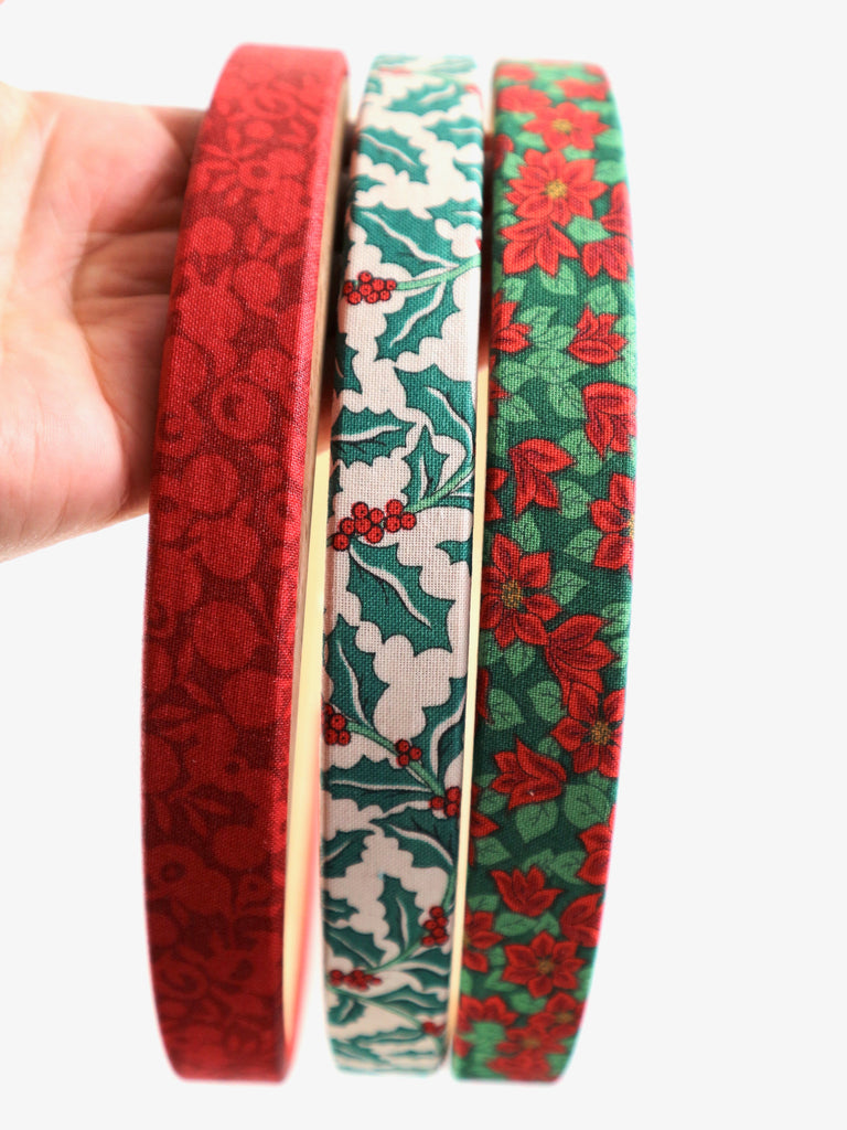 Three floral-patterned embroidery hoops held by a hand against a white background