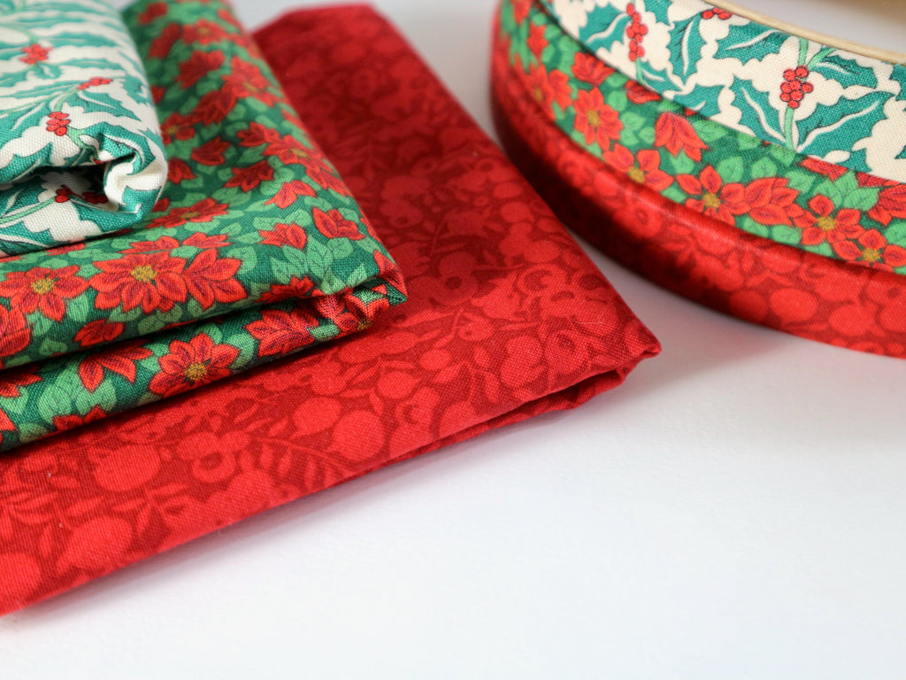 Red and green floral-patterned fabric on a white background with embroidery hoops