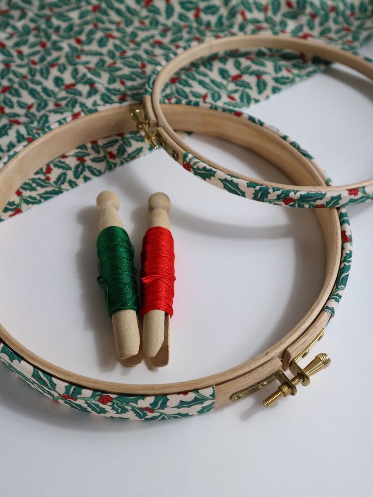Embroidery hoops with red and green thread on a holly patterned fabric background