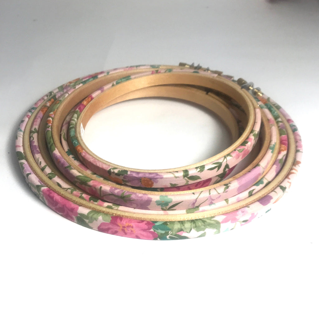 Stack of floral-patterned embroidery hoops on a pale pink background