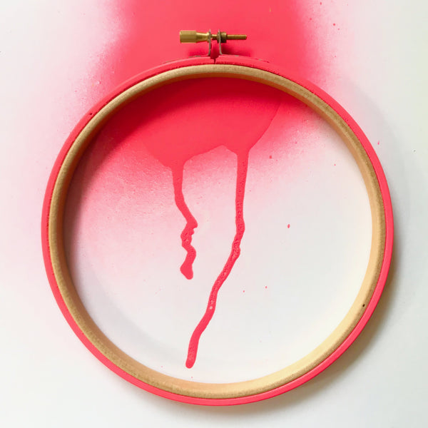 Red neon wooden embroidery hoop on a spray paint background.
