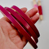 Fuchsia pink embroidery hoops in a hand with embroidery threads in the background.