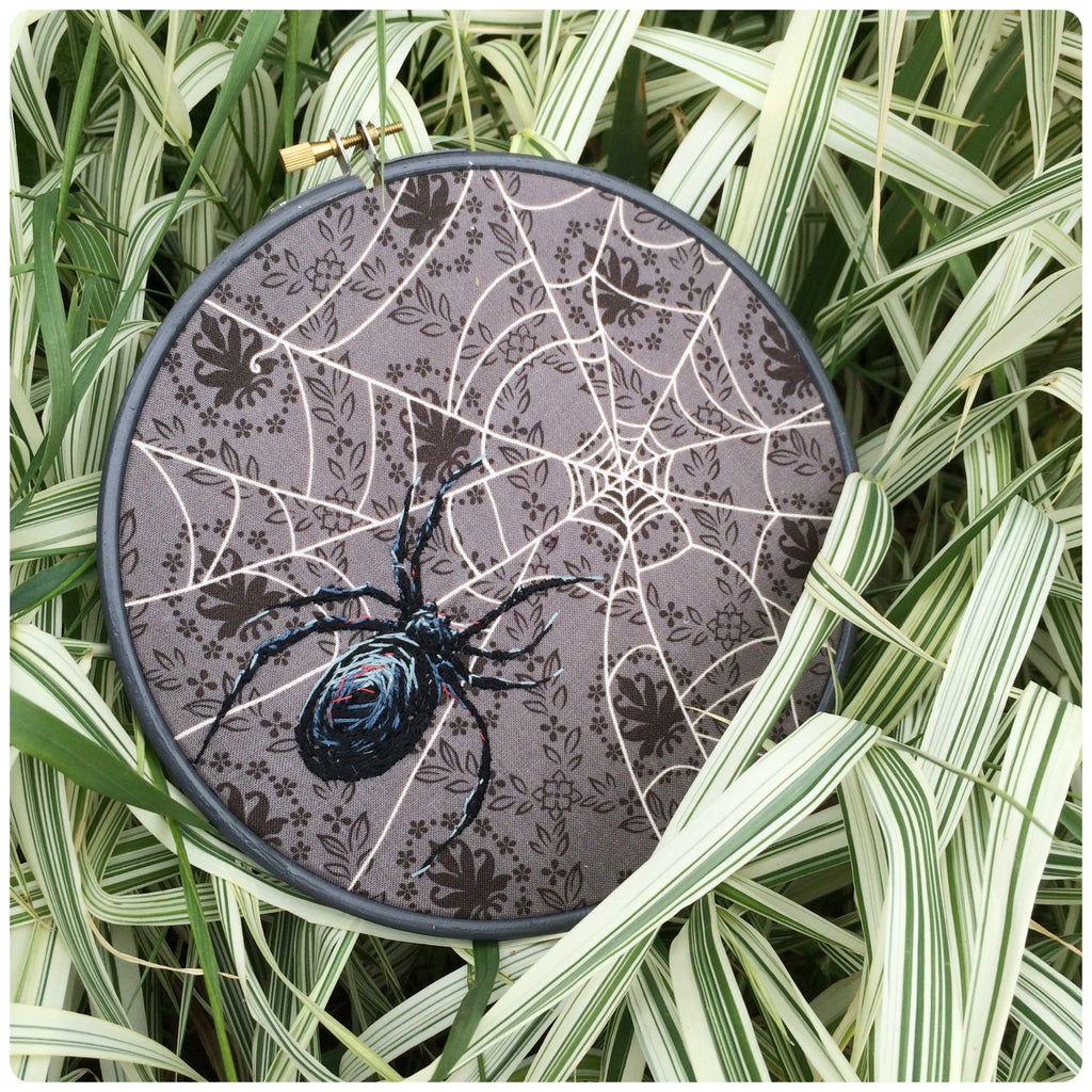 dark grey embroidery hoop framing a spider embroidery for halloween.