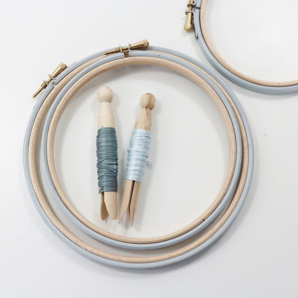 Pale grey embroidery hoops with embroidery threads on peg dolls.