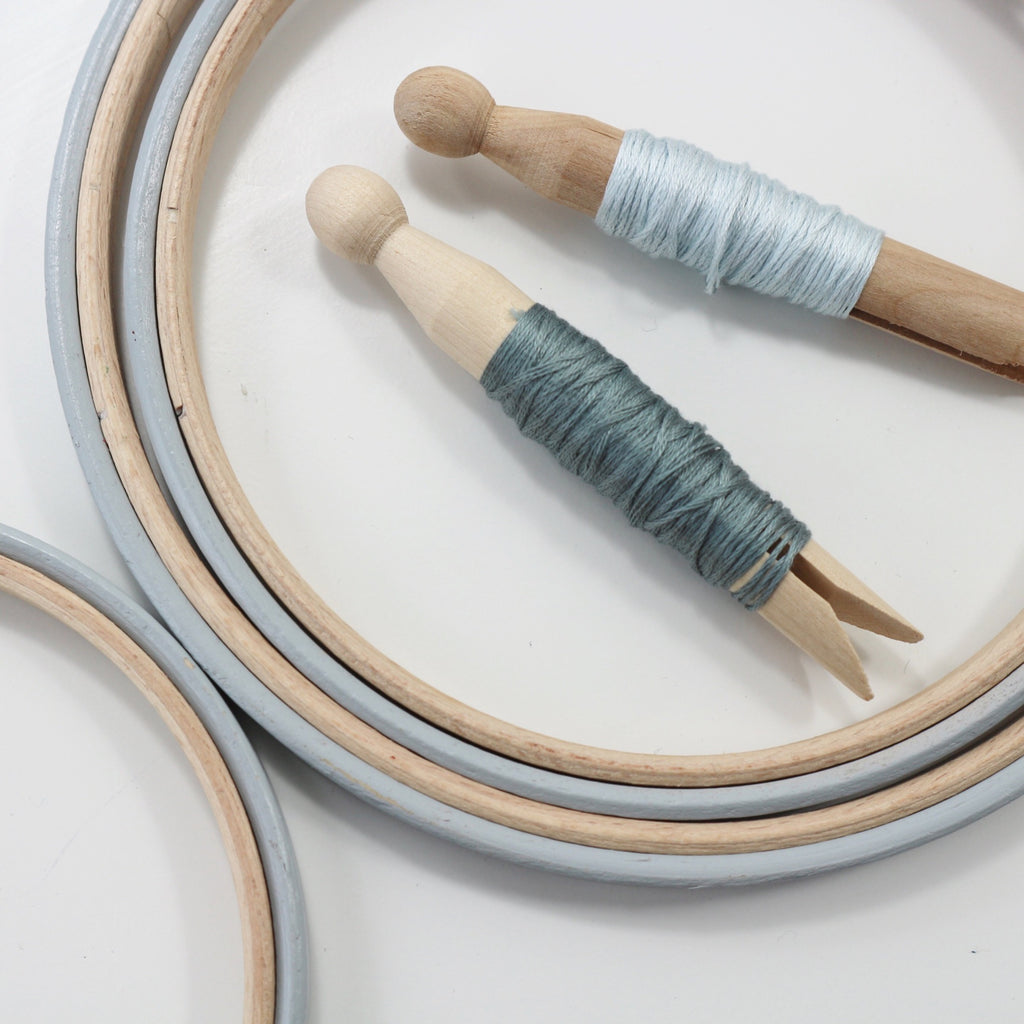 Light grey, hand painted embroidery hoops with embroidery floss on bobbins.