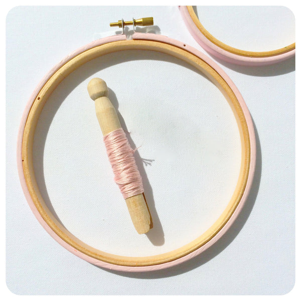 light pink embroidery hoop with thread bobbin.