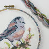 Purple and pink cross stitch bird and DMC embroidery threads.