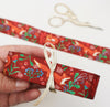Rust red grosgrain ribbon with flowers and berries, tied with a gold bow and held by a hand