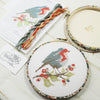 Ribin cross stitch on a branch of berries in a patterned  embroidery hoop.