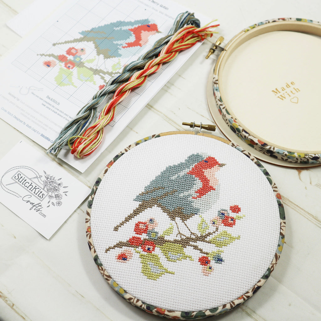 Ribin cross stitch on a branch of berries in a patterned  embroidery hoop.