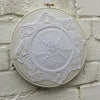 White on white embroidery in a white embroidery hoop on a white wall.