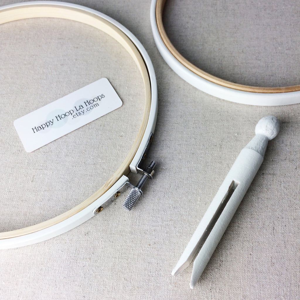 Two painted white embroidery hoops with a white wooden peg.